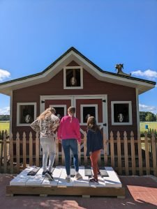 Three visitors playing a giant outdoor piano in front of a farm-themed playhouse