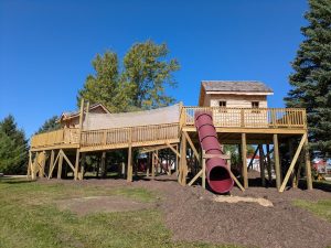 Elevated wooden playground with a net bridge and red tube slide