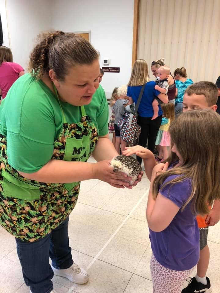 Animal educator holding a hedgehog while a child reaches out to pet it