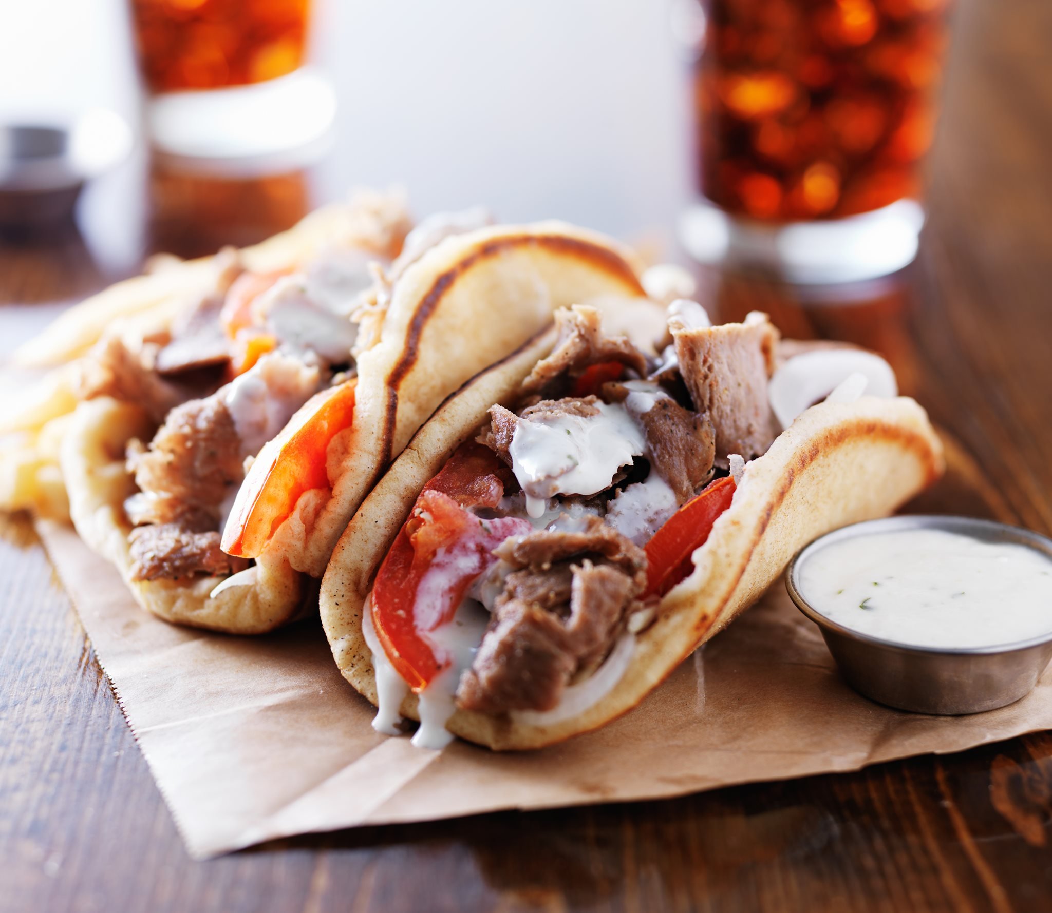 Two gyros filled with sliced meat, tomatoes, onions, and tzatziki sauce
