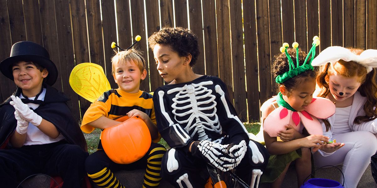 Five children in colorful Halloween costumes sitting together with trick-or-treat buckets